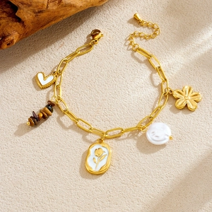 Gold charm bracelet featuring heart, baroque pearl, and floral pendants on wood background