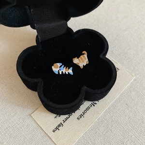 Detailed macro of cat and fishbone stud earrings inside a black floral jewelry box