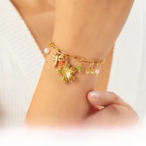 Detailed close-up of a gold-plated bracelet with dragonfly and cherry charms on a model