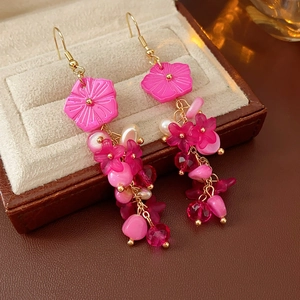 Détail de boucles d'oreilles fleur rose avec perles et pompons sur écrin à bijoux