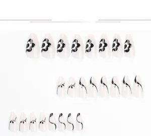 Detail view of almond press-on nails featuring black and white floral patterns and rhinestones