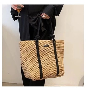 Close-up of khaki woven tote bag with black shoulder straps and magnetic closure