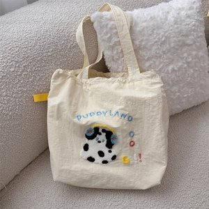 Detailed close-up of a cream canvas tote bag featuring an embroidered spotted puppy design