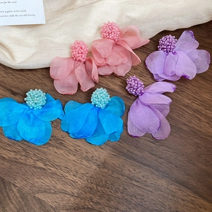 Detailed close-up of floral fabric earrings with seed bead centers on a rustic wooden table