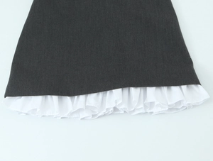 Detail of dark grey fabric featuring white ruffled hem layered dress construction