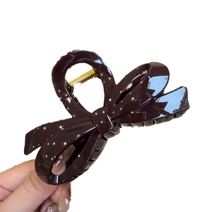 Brown bow-shaped hair claw clip in glossy finish held by a hand on white background