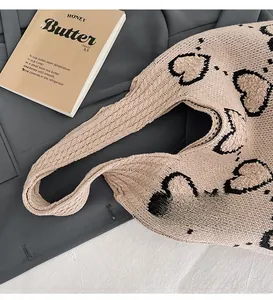 Détail du motif en maille torsadée avec cœurs noirs sur un grand sac beige