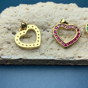 Golden heart pendants with rhinestones and red gemstone on beige stone background