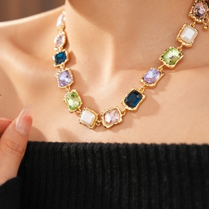 Detail of vintage gold necklace featuring colorful square gemstones on a model's collarbone