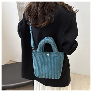 Detail showing blue corduroy texture and white button closure of the bucket bag