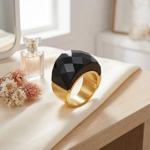 Detail of chunky gold ring with faceted black gemstone on elegant beige silk fabric