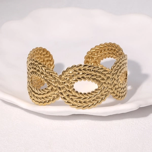 Luxurious gold stainless steel open cuff bracelet with intricate woven texture on ceramic tray