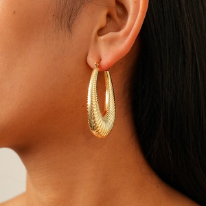 Close-up of golden oval hoop earrings with textured spiral ribbing on a model