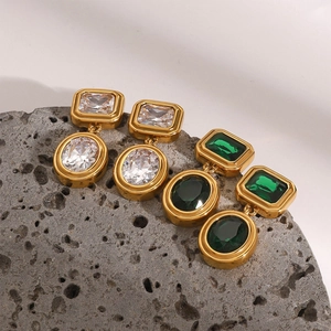 Detail of vintage gold earrings with green and clear zircon stones on grey rock