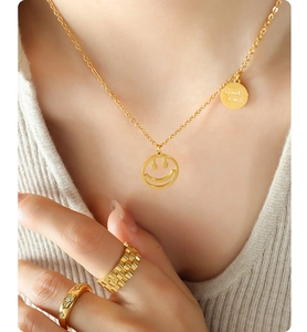 Detalle de collar dorado con colgante de carita sonriente y anillos en fondo de punto