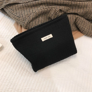 Close-up detail of black woven tweed cosmetic bag with simple wish label on bedding