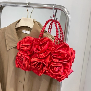 Detail view of red silk clutch bag featuring 3D fabric roses and beaded top handle