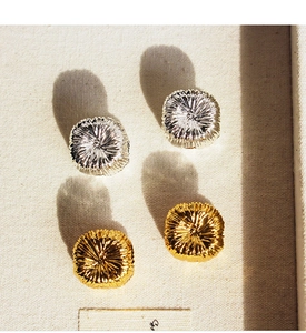 Macro shot of gold and silver pleated metal disk earrings on cream fabric background