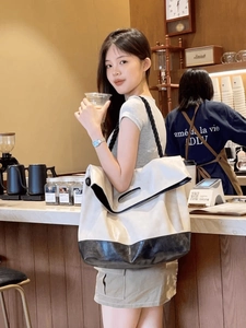 Close-up of beige canvas tote bag with black leather base and rope handles in a cafe setting