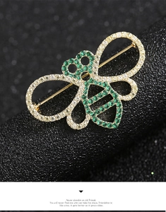 Macro view of gold bee brooch with inlaid zircons and pearls on textured black stand