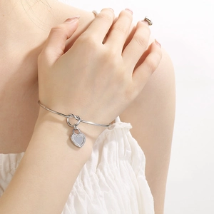 Polished stainless steel knot bracelet with heart pendant on model's wrist