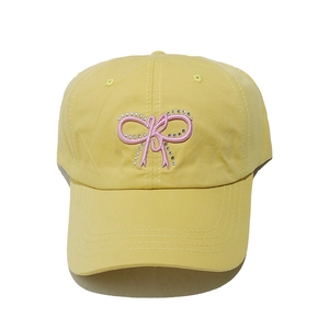 Detail of pink rhinestone bow embroidery on a pale yellow cotton twill baseball cap