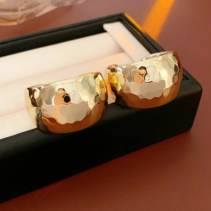 Macro view of wide C-shaped gold earrings with textured hammered finish on a jewelry box