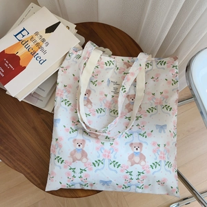 Détail du sac cabas en toile avec imprimés ours et fleurs posé sur une table en bois