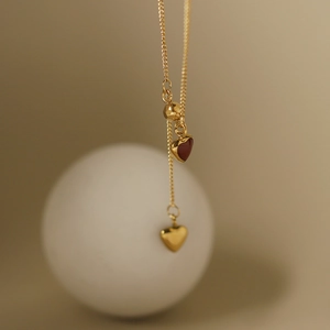 Close-up of gold chain featuring a red and gold heart pendant in a French vintage style