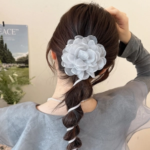 Détail d'une grande fleur en organza blanc avec de longs rubans sur une coiffure tressée