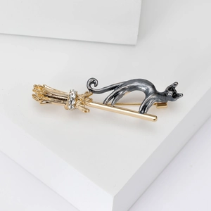 Detail of grey cat on golden broom brooch with sparkling rhinestones on white stands