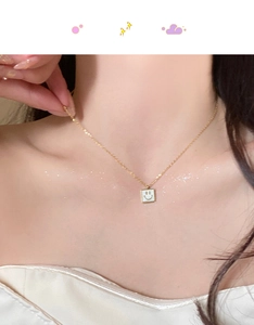 Close-up of gold chain necklace featuring a square white shell pendant with a black smiley face