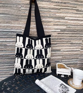 Detail of a knit tote bag with black and white rabbit patterns and black shoulder straps