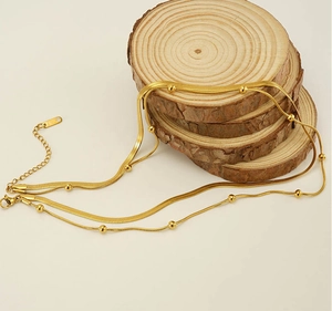 Detail einer goldenen zweilagigen Schlangenkette mit Perlen auf Holzscheiben