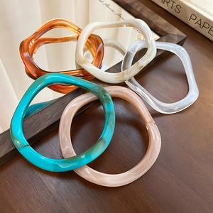 Close-up of wavy resin bangles in amber and marble tones on a rustic wooden desk