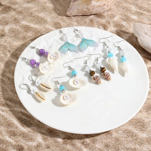 Ocean themed earrings featuring shell and starfish designs on a white plate with beach decor