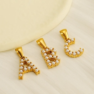 Golden 18K plated initial pendants A B C with pearl inlay on beige fabric background