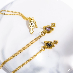 Detailed view of gold stainless steel necklaces with Saturn and star pendants on marble