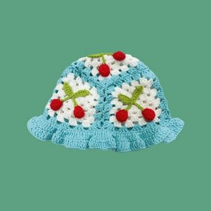 Detail of hand-knitted light blue bucket hat featuring red 3D cherries and wavy brim
