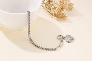 Detail view of silver Cuban chain bracelet with heart pendant on a white ceramic bowl