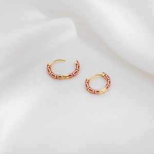 Close-up of golden hoop earrings with red enamel inlay on luxury white satin fabric