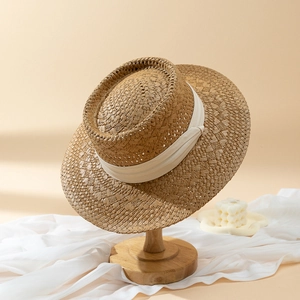 Flat top straw hat with cream ribbon on a wooden stand for sun protection and travel