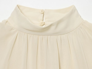 Detail of cream mock neck top featuring double resin button closure and pleated fabric