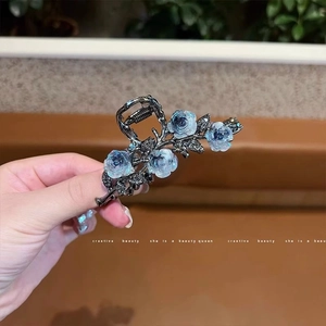 Détail de la pince à cheveux camélia en résine bleue avec finition en métal foncé et strass