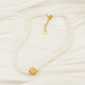 Elegant pearl necklace with golden textured sphere on cream silk fabric background