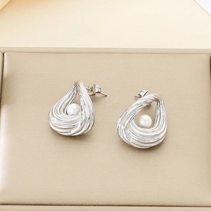 Detail of silver spiral teardrop earrings with white pearl inlay on a soft beige background