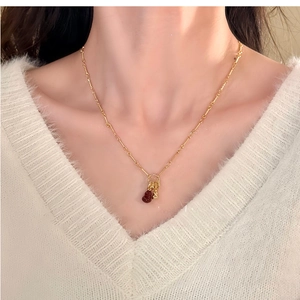 Detailed close-up of a double gourd gold plated necklace with a red stone on a model