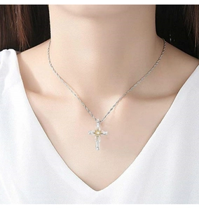 Close-up of a silver cross pendant necklace with gold accents worn by a model