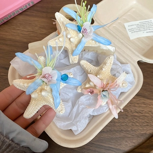 Detail of three starfish hair clips with fabric flowers and rhinestones held in hand