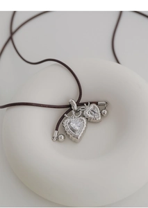 Detailed macro view of silver double heart pendants with clear zircons and brown woven cord